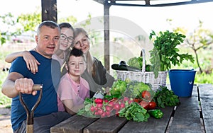 Smiling family sitting outdoors at table with harvested vegetables