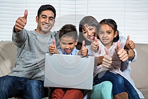 Smiling family on the sofa showing their thumbs up