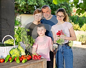 Smiling family standing on backyard with harvested vegetables