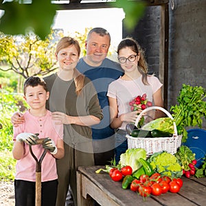 Smiling family standing on backyard with harvested vegetables