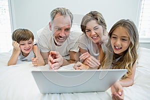 Smiling family using laptop on bed in bedroom