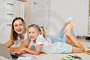 Smiling family using laptop computer together lying on floor in children room with modern light interior, looking at