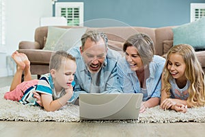 Smiling family using laptop while lying on carpet in living room