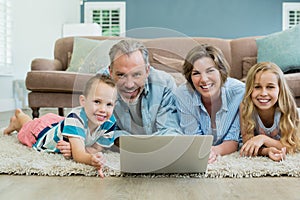 Smiling family using laptop while lying on carpet in living room