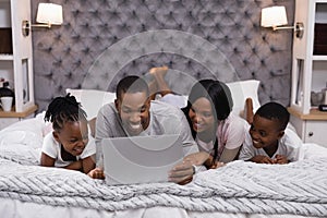 Smiling family using laptop while lying together on bed