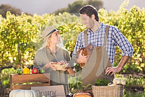 Smiling farmer couple holding chicken and eggs