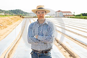 Smiling farmer standing on plantation mulched with polyethylene film