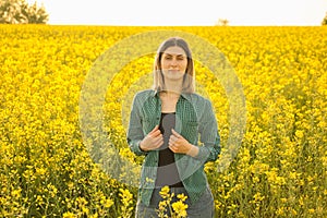 smiling farmer woman standing yellow flowering rapeseed and looking at camera