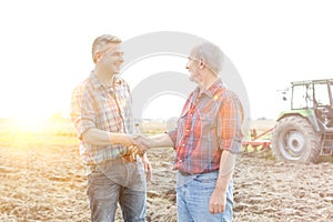 Smiling farmers shaking hands while standing on field at farm