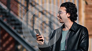 Smiling fashion Arab guy use smartphone mobile phone message chatting outdoor with positive emotion