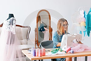 Smiling fashion designer looking at camera at workplace, dressmaker, needlewoman or tailor shop owner sitting at desk with color