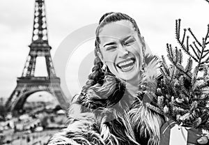 smiling fashion-monger with Christmas tree taking selfie in Paris