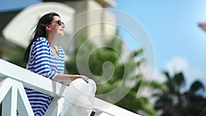 Smiling fashion woman relaxing on balcony of luxury hotel resort enjoying summer travel vacation