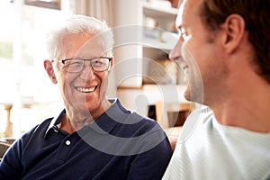 Smiling Father With Adult Son Relaxing On Sofa At Home