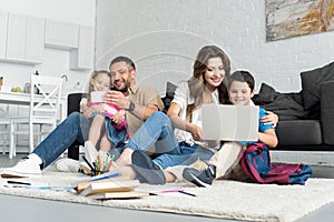 smiling father and daughter taking selfie on smartphone while mother and son using laptop together