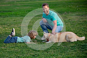 Smiling father and his son playing with dog in park with pet. Boy child walk with doggy.