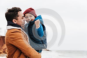 Smiling father holding son in his arms while spending fun time together on beach