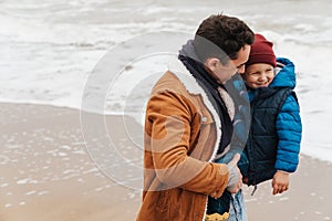 Smiling father holding son in his arms while spending fun time together on beach