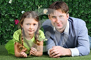 Smiling father and little daughter lie on green lawn