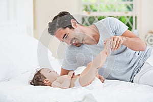 Smiling father playing with baby on bed