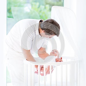 Smiling father putting his newborn baby in crib