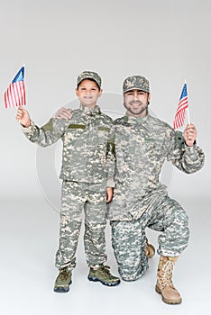 smiling father and son in camouflage clothing with american flagpoles in hands