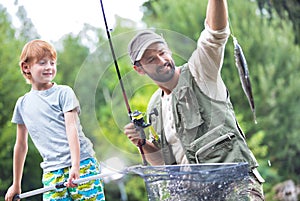 Smiling father and son catching fish on pier