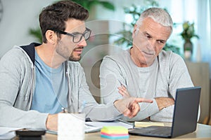 smiling father and son with laptop while sitting at desk photo