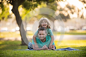 Smiling father and son laying on grass in summer park outdoor. People having fun outdoors. Concept of happy vacation and