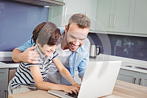 Smiling father and son working on laptop