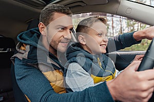 smiling father teaching cute little son driving car
