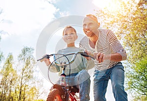 Smiling father teaching his daughter to ride a bicycle. They enjoy togetherness in the summer city park. Happy childhood concept