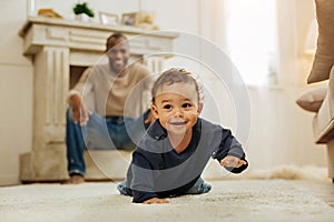 Smiling father watching his son crawling