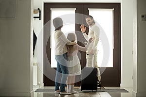 Smiling father waving goodbye to wife and daughter leaving home photo