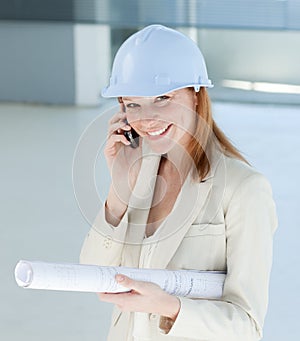 Smiling female architect with hardhat on phone