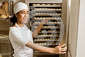 smiling female baker pointing at dough inside of industrial oven
