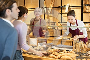 Smiling female bakers in maroon aprons working behind counter