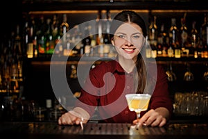 Smiling female bartender serving a delicious yellow cocktail