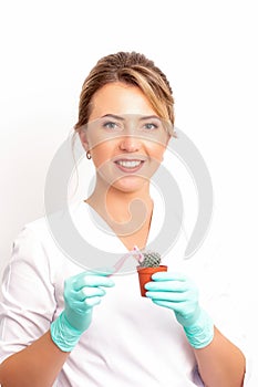 A smiling female beautician holds little green cactus with the razor in her hands. Hair removal concept.