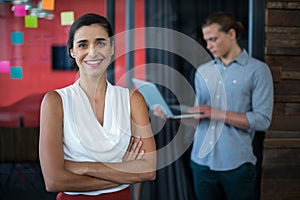 Smiling female business executive standing with arms crossed in office