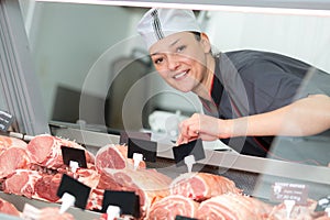 smiling female butcher labelling joints meat in counter