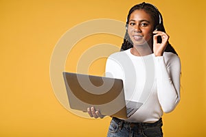 Smiling female call center worker wearing wireless headset, working laptop. Cheerful young woman working or studying