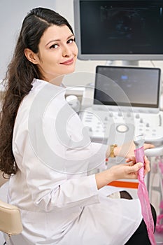 Young nurse working on ultrasound scanner, looking at camera