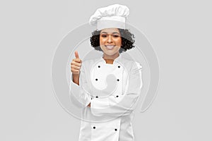smiling female chef in jacket showing thumbs up