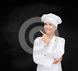 Smiling female chef pointing finger to something