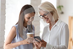 Smiling female colleagues browse smartphone at office coffee break photo