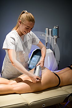 Smiling female cosmetologist performs an anti-cellulite massage on the client& x27;s buttocks using an endomassage device