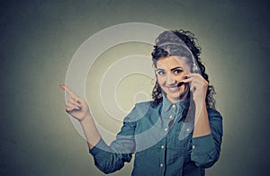 Smiling female customer representative with phone headset pointing at copy space