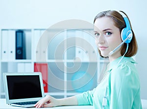 Smiling female customer support phone operator sitting at office workplace half turn looking in camera portrait.