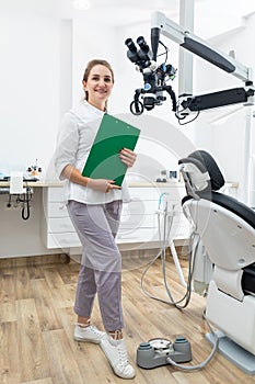 Smiling female dentist holding clipboard with patient records in hands at dental clinic